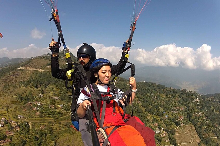 A person paragliding with a guide, over a mountainous landscape with terraced fields. 3