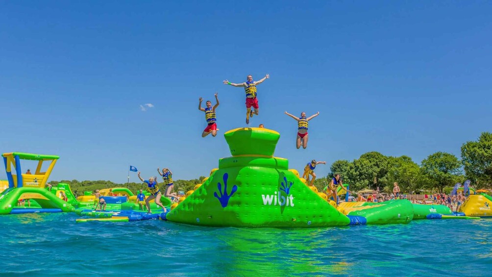 People jumping off a green inflatable structure into a pool. 4