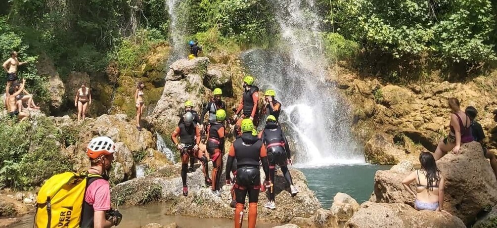 A group of people in a rocky outdoor setting with a waterfall. 5