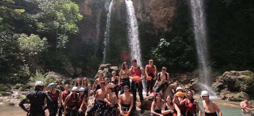 A group of people gathered around a waterfall in a forested area. 1
