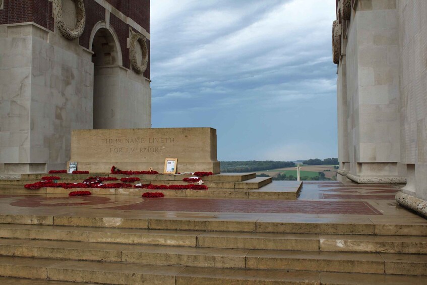A memorial with inscriptions, red flowers, and a cross. 1