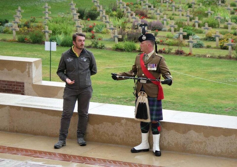 A person in a kilt and military uniform standing in a cemetery with crosses in the background. 5