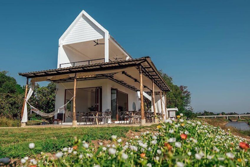 A white house with a porch, surrounded by a field of flowers and a river in the background. 5