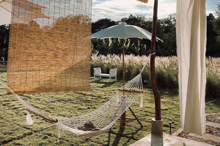 A hammock, a white umbrella, and a white chair in a grassy outdoor area. 2