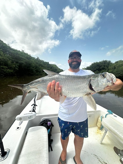 A person holding a large fish on a boat with a river and green hills in the background. 1