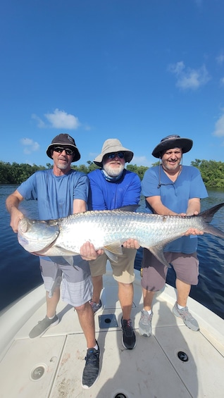 Three people on a boat holding a large fish. 5