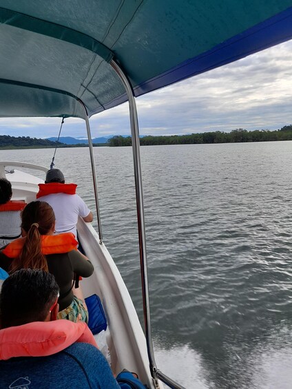 A boat with passengers wearing life jackets, calm water, and a forested shoreline in the background. 2