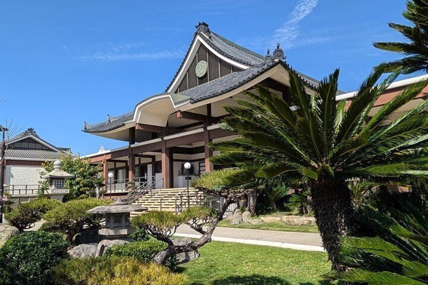 Edificio japonés tradicional con techo curvo, rodeado de exuberante follaje y un farol de piedra. 5