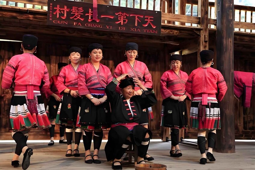 A group of people in traditional attire performing a dance in front of a wooden building with a sign in a foreign language. 1