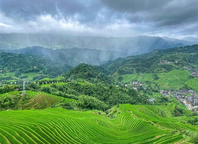 Terraced green fields, a power line tower, and a small village in a mountainous area. 3