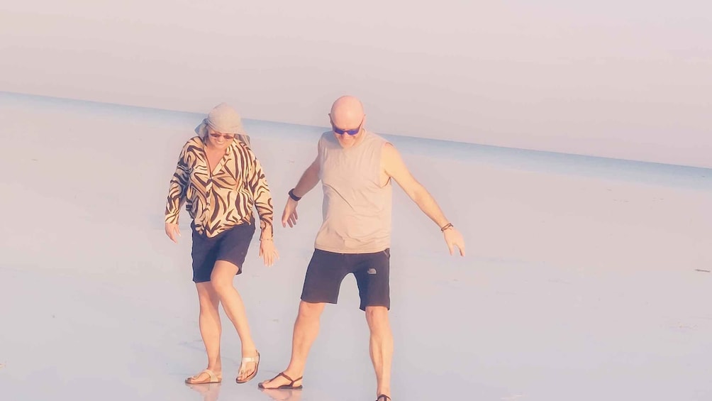Two people walking on a beach with a clear sky. 1