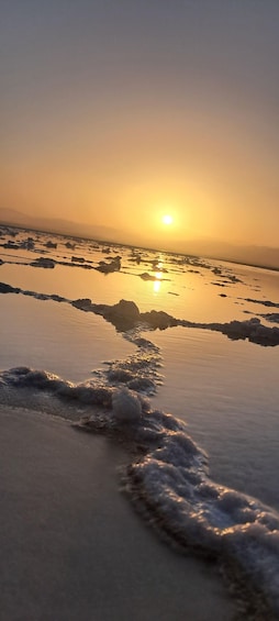 A sunset over a salt flat with scattered rocks and gentle waves. 3