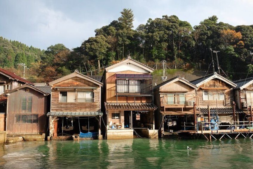 Wooden houses by a calm river, surrounded by trees. 1