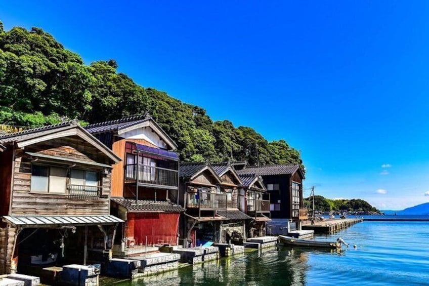 Traditional wooden houses by a calm lake with a forested hillside in the background. 2
