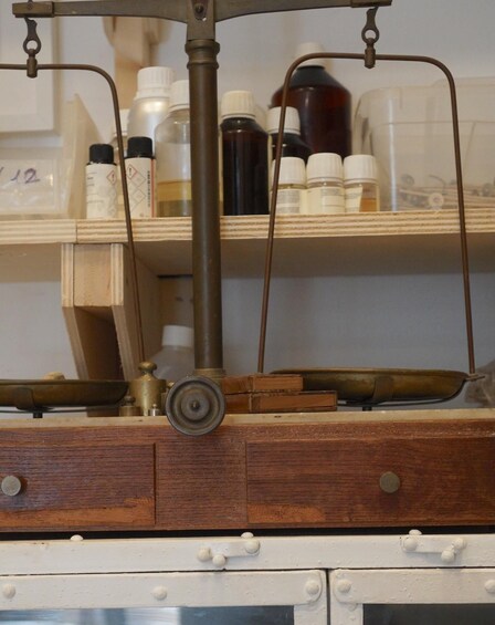 A wooden cabinet with drawers, a brass scale, and shelves holding various bottles. 4