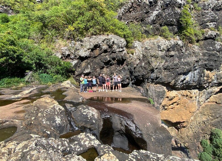 A group of people standing on a rocky outcrop by a small body of water surrounded by greenery. 2