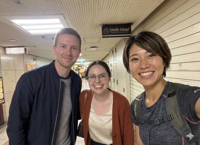Three people in a hallway with a sign reading 'Smile-Hand.' 1