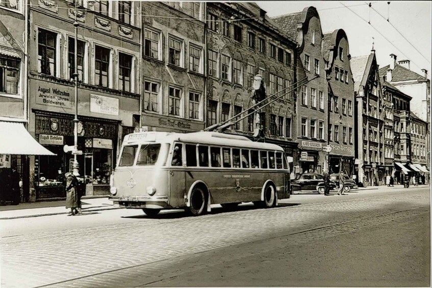 A vintage tram on a cobblestone street with pedestrians and classic architecture. 1