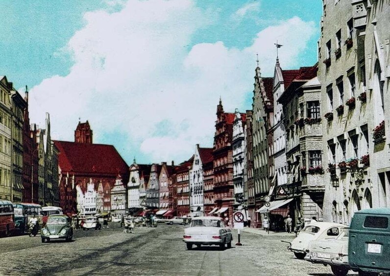 A cobblestone street lined with historic buildings, a vintage car, and a tram. 4