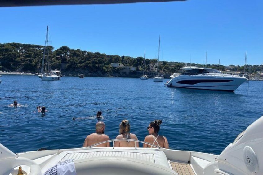 Ein Boot mit Personen auf dem Deck, eine Marina voller Boote und eine Küstenlinie mit Gebäuden. 5