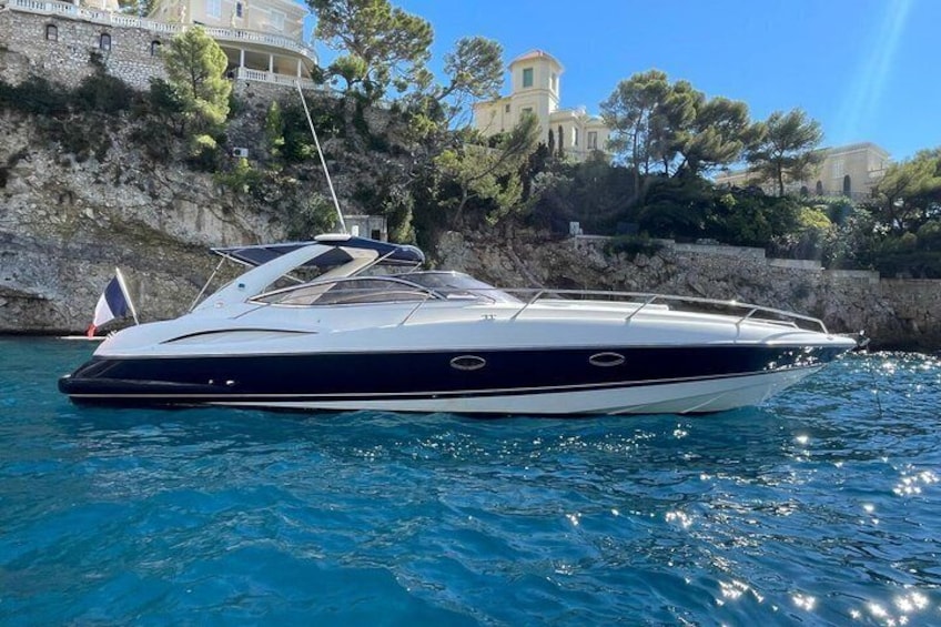 Eine Yacht liegt an der Küste bei Felsen, im Hintergrund ist ein Gebäude zu sehen. 1