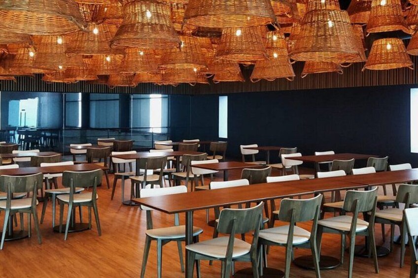 A conference room with tables and chairs, a dark wall, and woven ceiling lights. 3