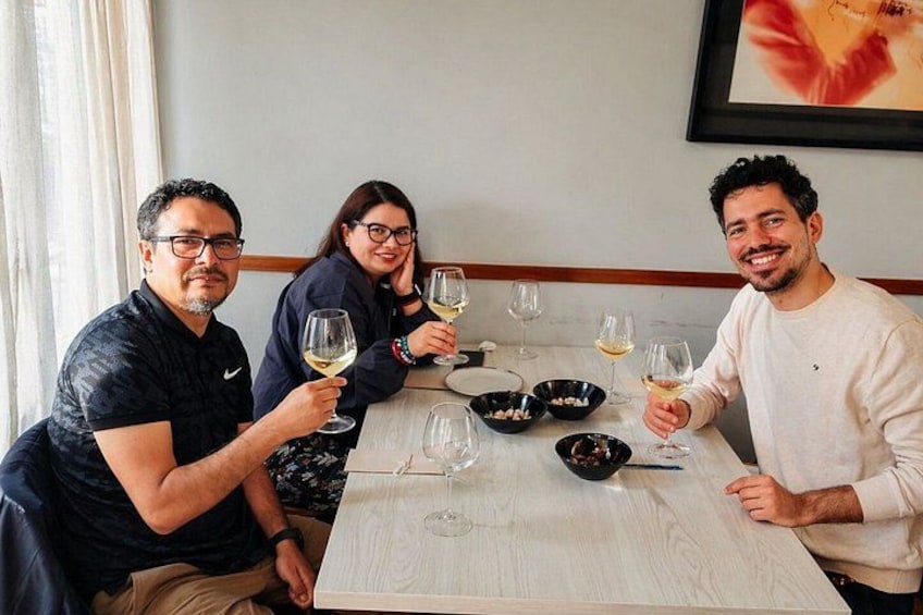 Three people sitting at a table with wine glasses, bowls, and a menu. 4