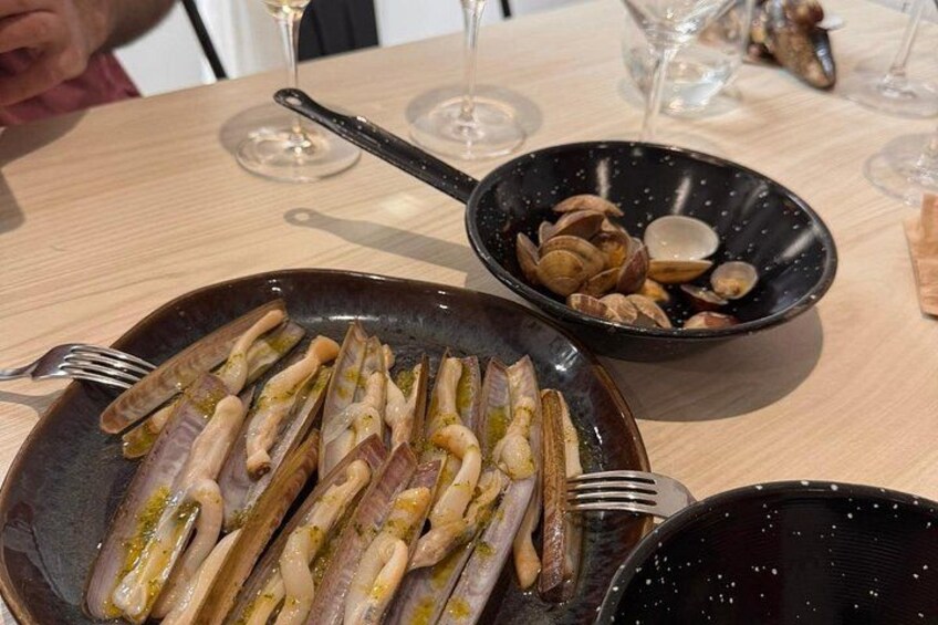 A dining table with plates of food, wine glasses, and a bowl of clams. 2