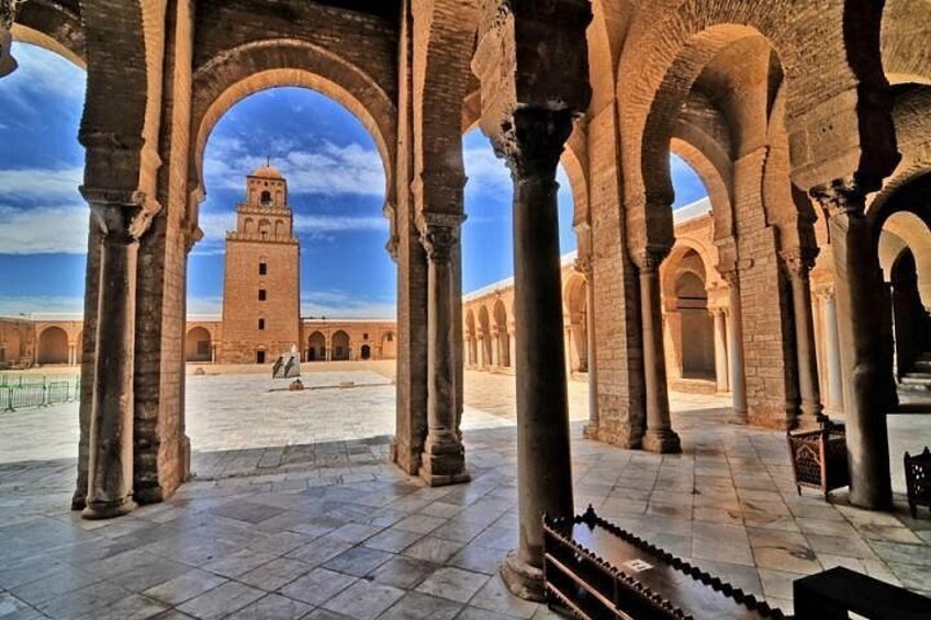 Una estructura arquitectónica con arcos y columnas, una torre al fondo y un cielo despejado. 1