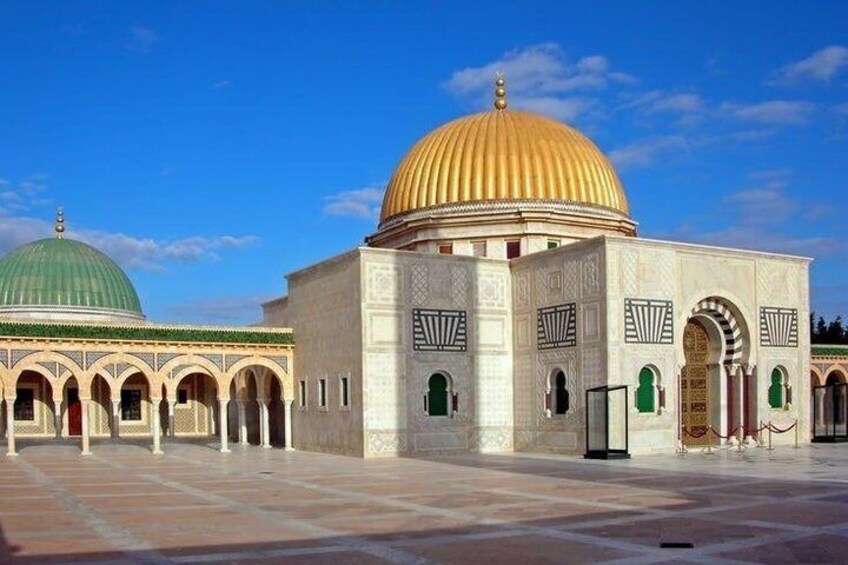 A mosque with a large golden dome and green dome, surrounded by a courtyard with tiled flooring. 3