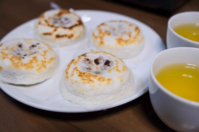 A plate with four dumplings and two cups of soup. 1
