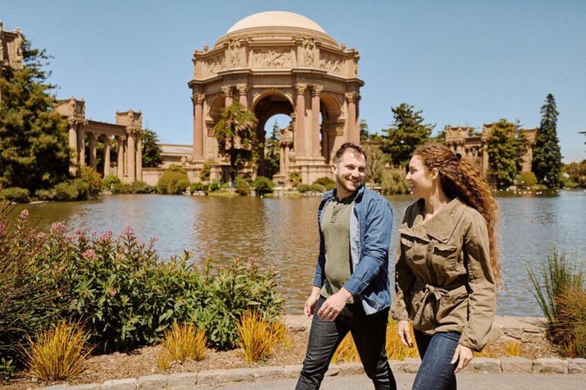 A couple walking by a historic fountain with a large archway and a lake in the background. 5