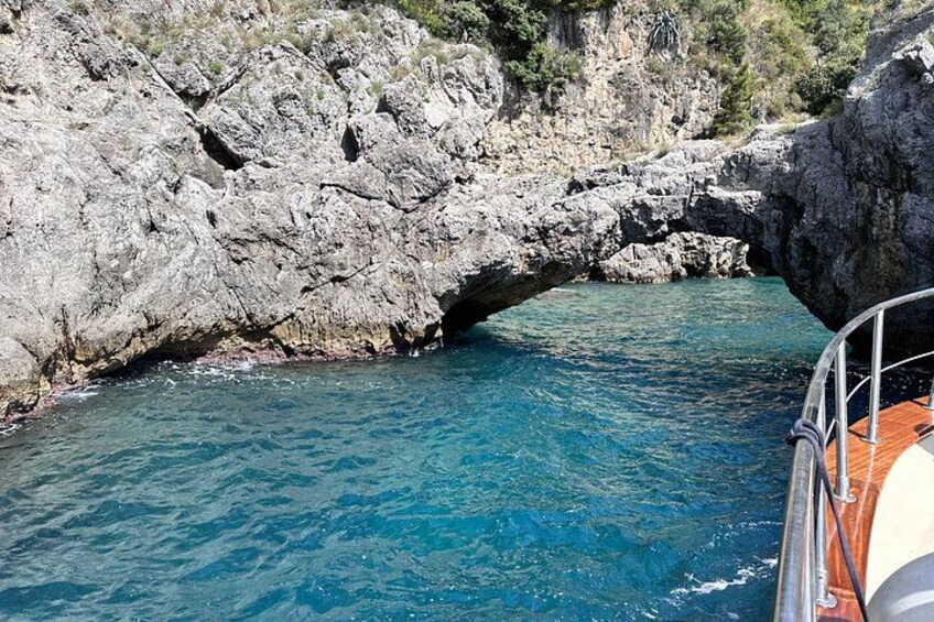 A rocky coastal landscape with a natural arch formation over clear blue water. 2