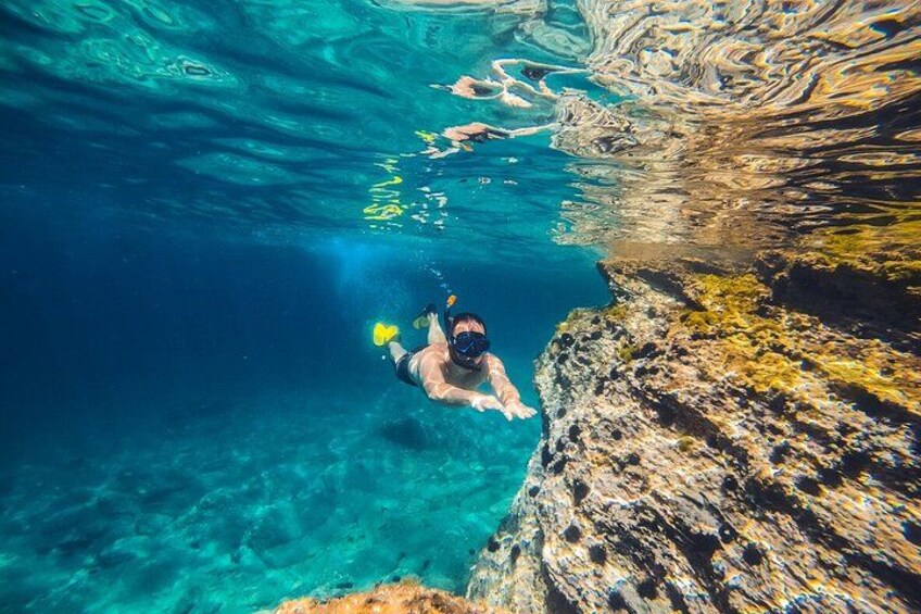 A person snorkeling underwater near a rocky cliff. 5