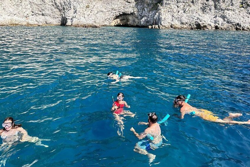 People snorkeling in clear blue water with rocky cliffs in the background. 3