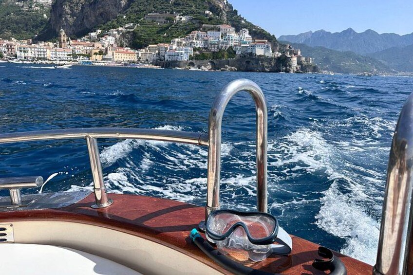 A boat with metal railings, a diving mask, and a snorkel on the deck. In the background, there is a coastal town with buildings and mountains. 4
