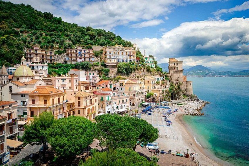 A coastal town with terraced buildings, a beach, and a historic tower. 1