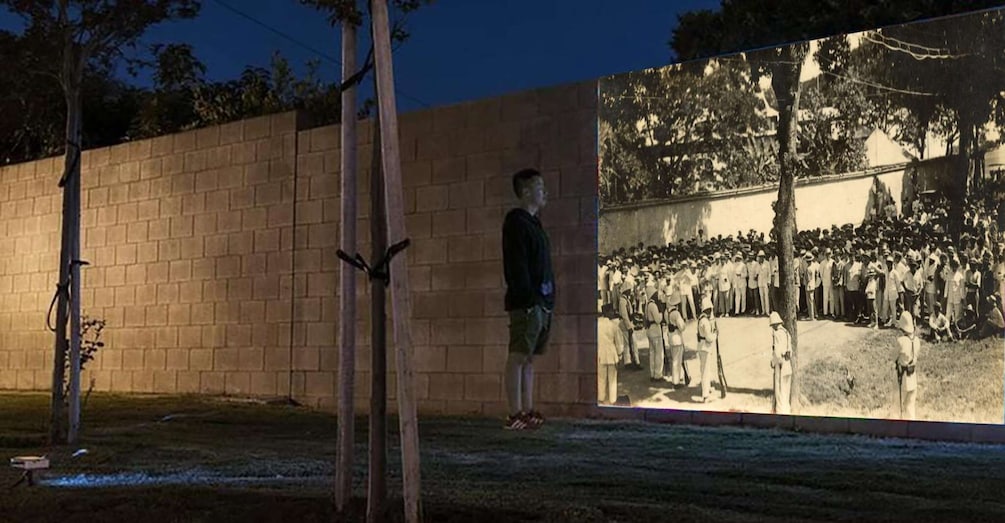 A person standing in front of a brick wall with a mural depicting a historical military scene. 1