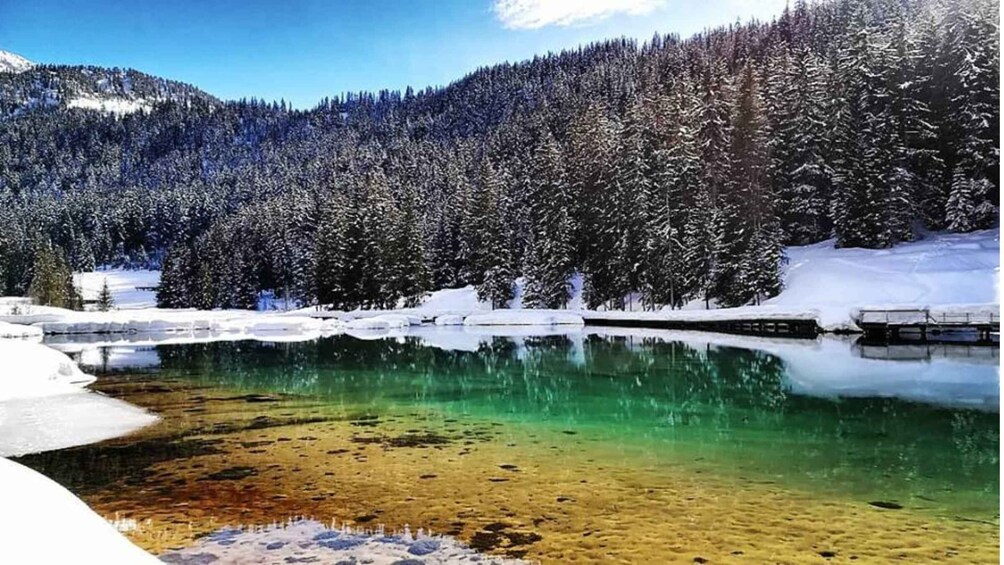 A clear lake surrounded by snow-covered trees and mountains. 1