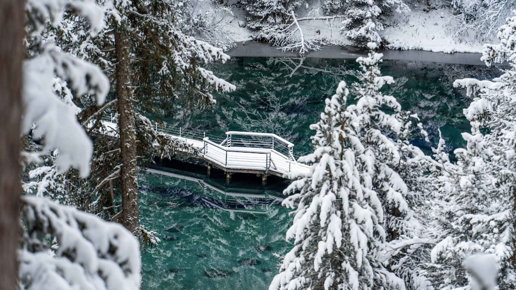 A snow-covered bridge over a clear body of water, surrounded by snow-laden trees. 3