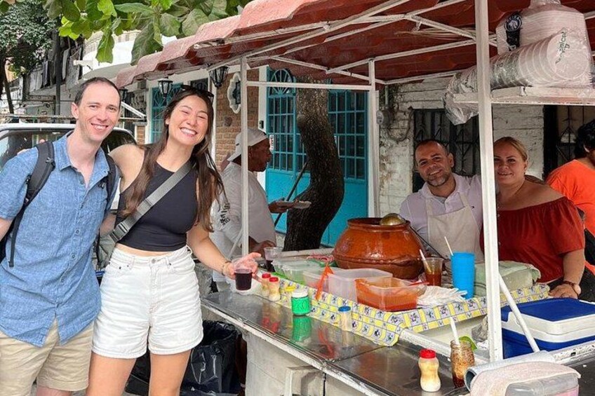 A street food stall with a large clay pot, a table with condiments, and a person serving food. 5