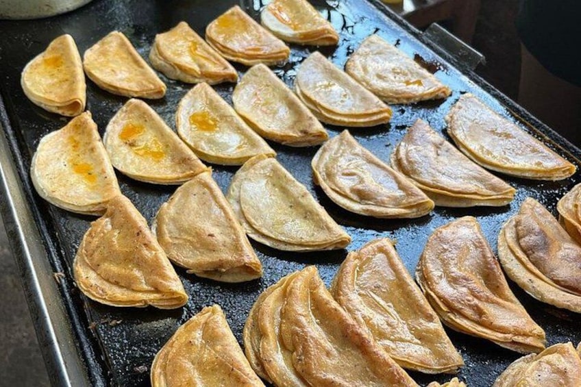 A tray of triangular pastries being cooked on a griddle. 2