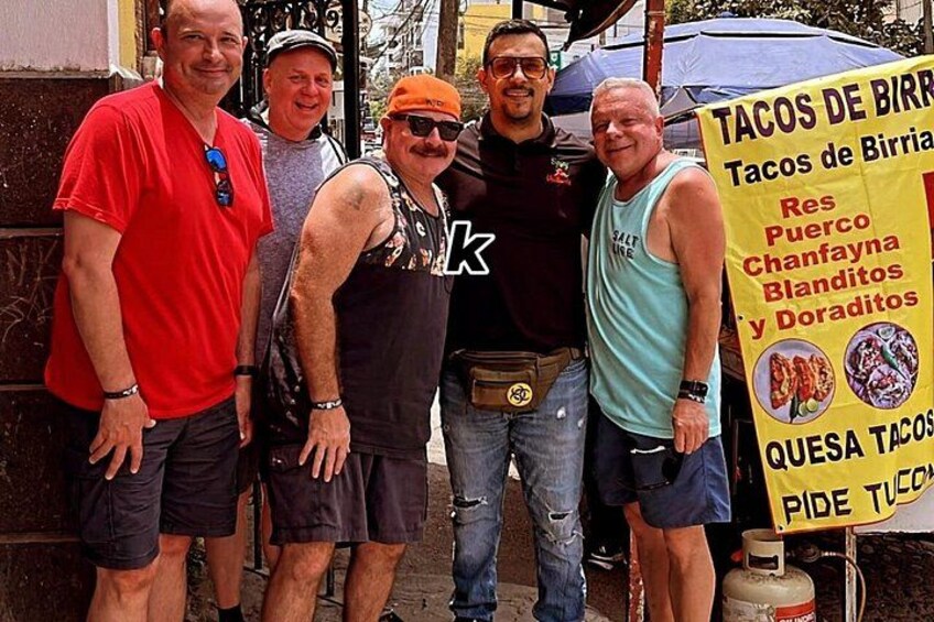 A group of people standing in front of a food cart with a sign listing items like tacos and quesadillas. 3
