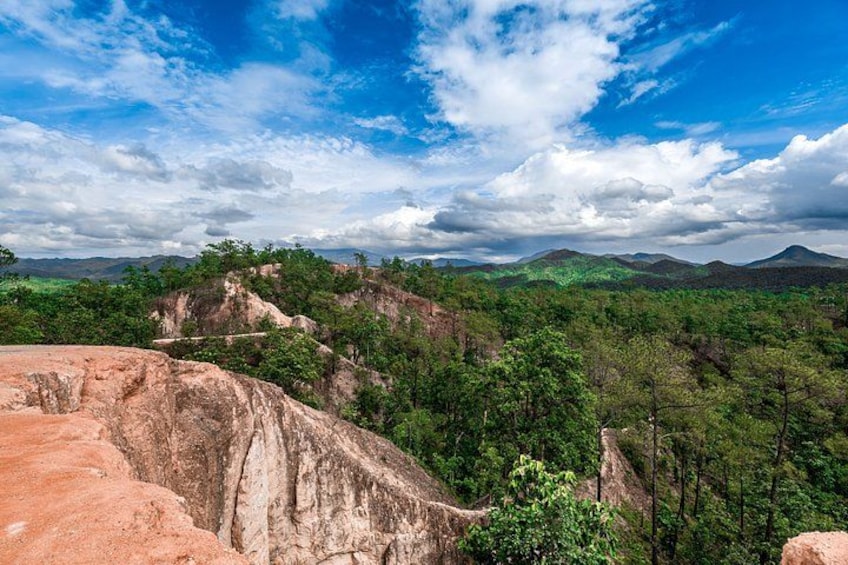 A mountainous landscape with dense green forests and rocky outcrops under a partly cloudy sky. 5