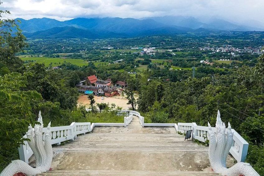 A viewpoint overlooking a village with a prominent house, lush greenery, and distant mountains. 4