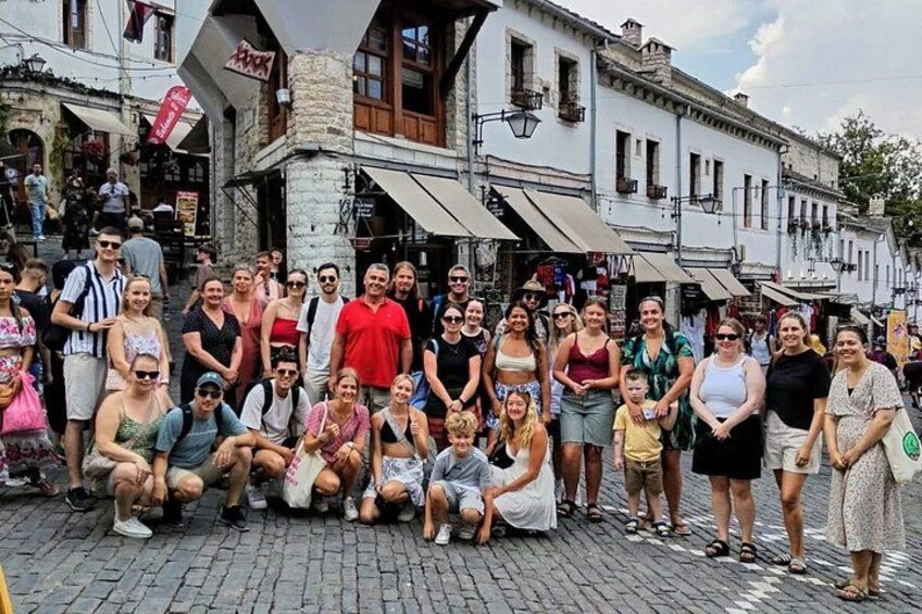 En gruppe mennesker poserer til et billede på en brostensbelagt gade med historiske bygninger i baggrunden. 1