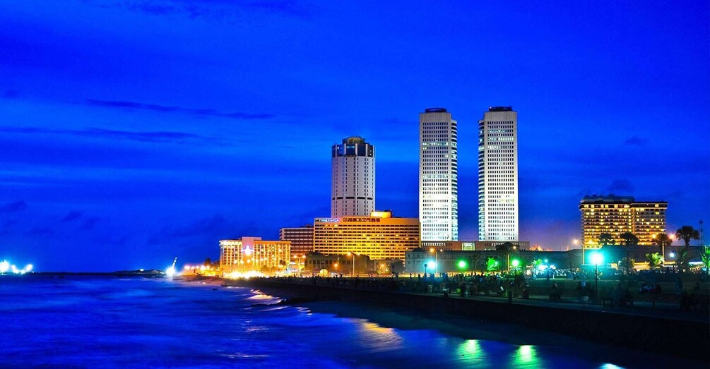 A city skyline with illuminated buildings and a coastline at dusk. 1