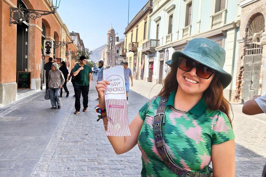 A person holding a sign with text, standing on a cobblestone street with historic buildings in the background. 4