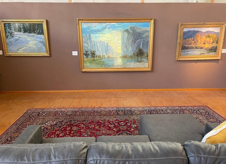 An art gallery with three framed paintings on the wall and a patterned rug on the floor. 1