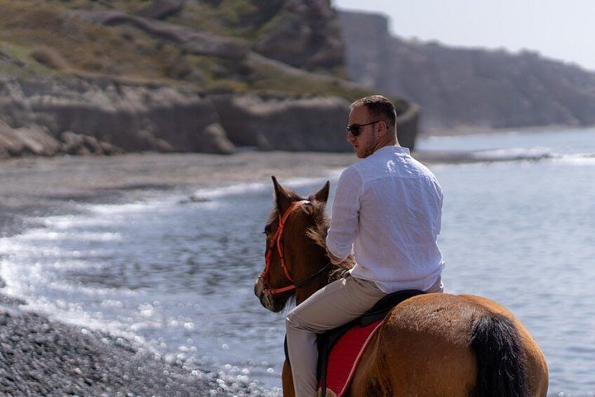 A person riding a horse along a rocky shoreline with cliffs in the background. 4